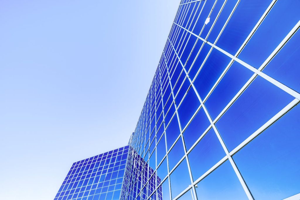 Low angle of modern high rise skyscraper with glass walls placed in city under cloudless blue sky in sunny day