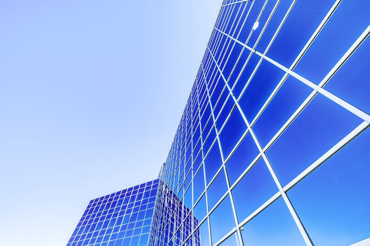 Low angle of modern high rise skyscraper with glass walls placed in city under cloudless blue sky in sunny day